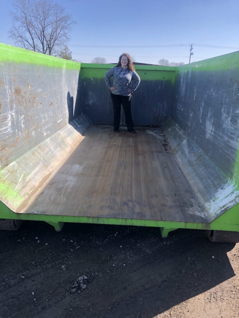 A woman standing in an empty 20 yard dumpster.